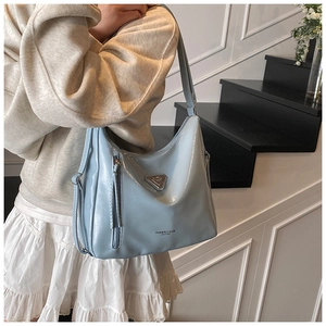 Détail du sac hobo bleu clair avec logo métallique et pompons décoratifs sur le côté