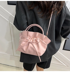 Detailed view of pink cloud bag with bow accent worn over a dark oversized blazer