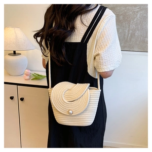 Détail du sac seau tissé crème avec boucle en perle, porté par un mannequin en décor épuré