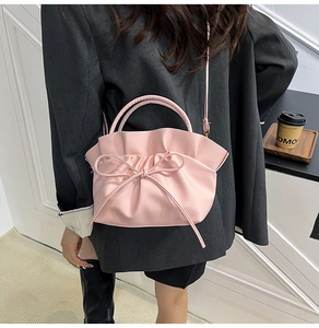 Detailed view of pink pleated tote bag with bow accent on a model in a grey blazer