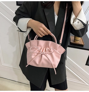 Detailed close-up of pink cloud-shaped handbag with bow accent worn by model in gray suit