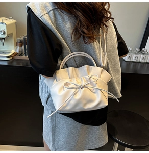Close-up of white ruched tote bag with bow detail, showing top handle and shoulder strap