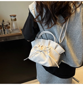 Detail of white pleated tote bag with bow accent shown in a warm cafe setting