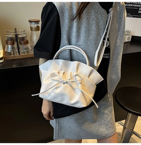 Detail of white ruffled cloud bag with bow, worn crossbody by a model in a cafe