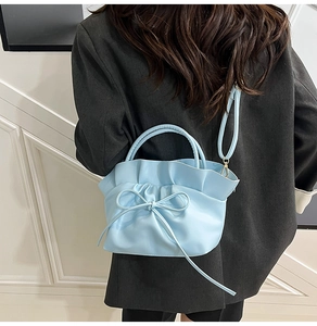 Close-up of light blue ruffled cloud bag with bow detail worn with dark blazer