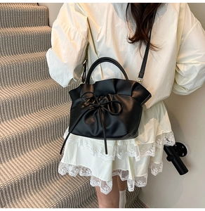 Detail of black pleated cloud bag with bow accent shown as crossbody on model