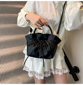 Close-up of pleated bow detail and matte leather texture on a black crossbody tote bag