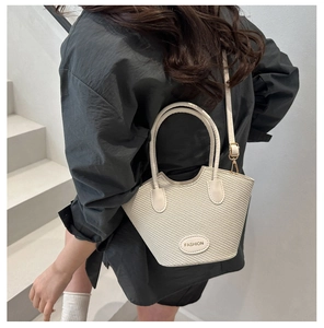 Detail of cream woven bucket bag featuring round handles and Fashion brand leather patch