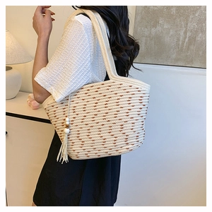 Detail view of woven straw tote bag featuring white wood beads and fringe tassel pendant