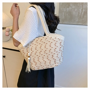 Detail of hand-woven straw tote bag with brown polka dot pattern and tassel charm
