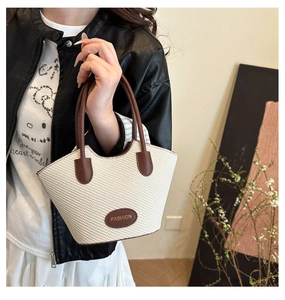 Detail of hand-woven straw tote bag with brown leather trim and golden fashion logo