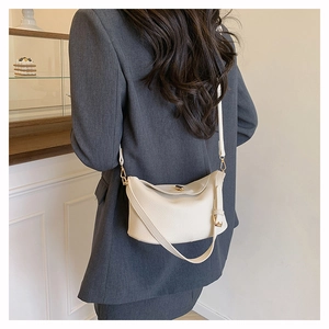 Detail of off-white lychee grain leather handbag with gold metal clasp on model