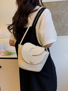 Sac seau en paille beige à fermoir perle porté par un mannequin pour les vacances d'été