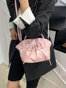 Pink pleated cloud tote bag with bow detail worn by model over a grey blazer