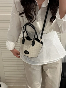 Beige woven bucket bag with black leather handles and crossbody strap for women