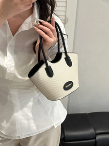 Women's chic contrast straw bucket bag with black trim and fashion plaque held by model
