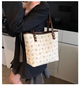 Detail of a large cream tote bag with brown straps and floral logo pattern