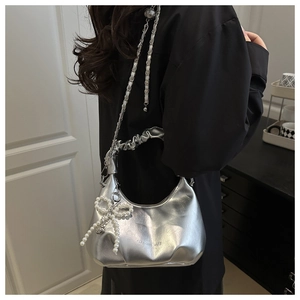 Close-up of silver leather handbag with pearl bow pendant and metal chain strap detail