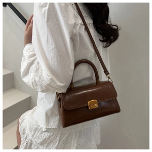 Brown leather crossbody bag shown on model's side with gold clasp and lace dress