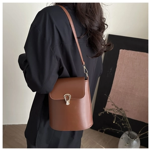 Detail of dark brown bucket bag featuring a gold horseshoe buckle on model with black top