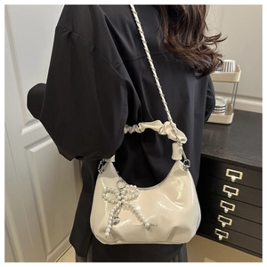Détail du sac hobo en cuir verni blanc crème avec breloque nœud perlé à l'épaule