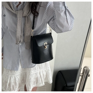 Detail view of black leather bucket bag featuring a golden shield-shaped metal buckle lock