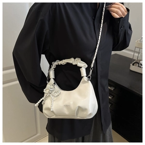 Détail du sac plissé blanc avec pendentif nœud en perles et bandoulière chaîne argent