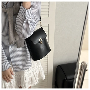 Detail of black leather bucket bag featuring a gold horseshoe buckle and retro design