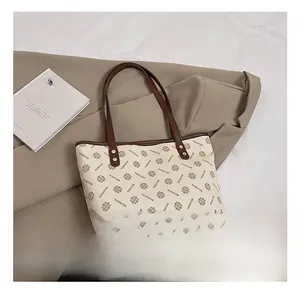 Detail view of printed tote bag with brown straps, golden rivets and brand pattern