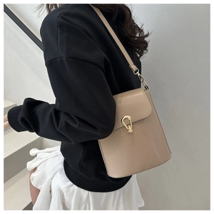 Detail of minimalist beige bucket bag featuring a gold teardrop twist lock and leather texture