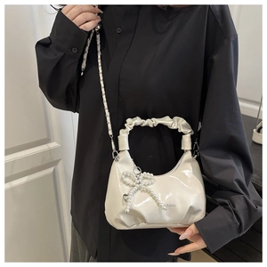 Detail of cream glossy patent leather handbag with pearl bow charm and pleated handle