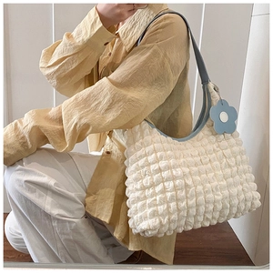 Close-up of white bubble texture tote bag with blue strap and daisy charm accessory