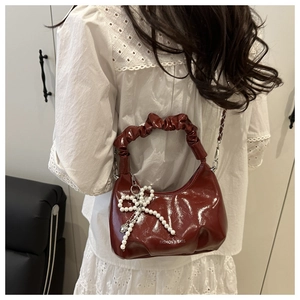 Detail of burgundy crescent bag with ruched handle and pearl bow charm accessory