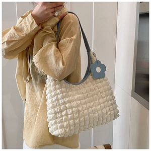 Detail of popcorn fabric texture on a cream shoulder bag with a blue floral charm
