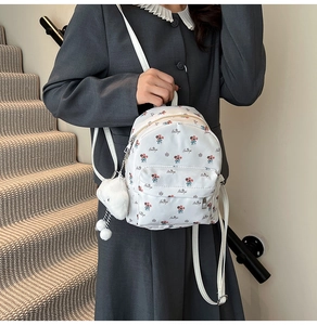 Détail d'un mini sac à dos floral avec breloque nuage en peluche et sangles blanches