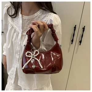 Close-up of wine red glossy handbag with pearl bow pendant and pleated handle
