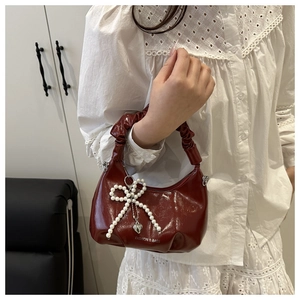 Detail of burgundy patent leather bag with ruched handle and pearl bow charm accessory