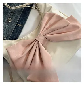 Detail view of a creamy white handbag featuring a large satin pink bow and metal strap clips
