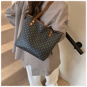 Close-up of black patterned tote bag with brown leather straps and gold rivets