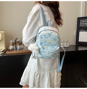 Détail d'un sac à dos bleu clair à fleurs avec petit pendentif en forme de nuage