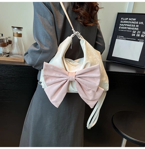 Detail of a beige leather tote with a large pink velvet bow worn by a model in a cafe