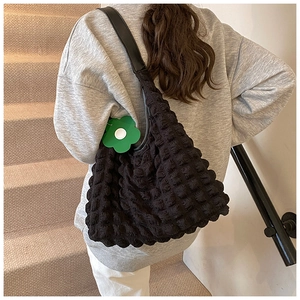 Detail of black bubble texture tote bag with green floral pendant on shoulder