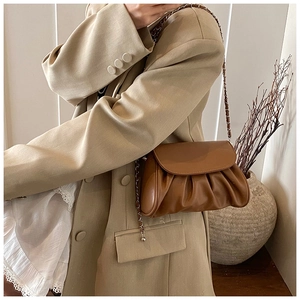 Detailed view of brown ruched cloud bag with light gold woven chain strap on model