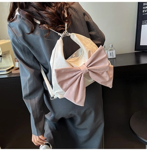 Detail of a cream crescent bag with a large pink velvet bow worn by a model in a cafe
