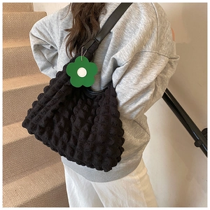 Detail of black bubble textured tote bag with a green floral pendant on shoulder strap