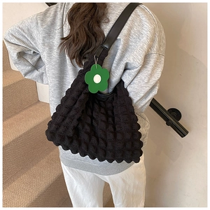 Détail d'un sac cabas noir à texture bulle avec un pendentif floral vert décoratif