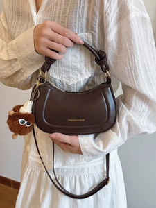 Dark brown half-moon underarm bag with knot handle and plush charm on striped shirt