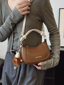Brown leather saddle bag with white ruched handle and fuzzy ball charm pendant
