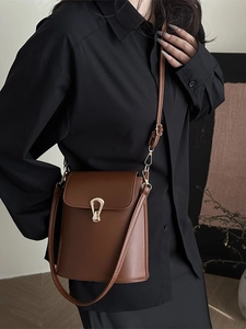 Deep brown bucket bag with gold horseshoe clasp shown from a stylish cross-body perspective