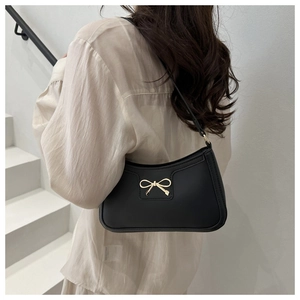 Black leather underarm bag with gold bow accessory worn by model on a white staircase
